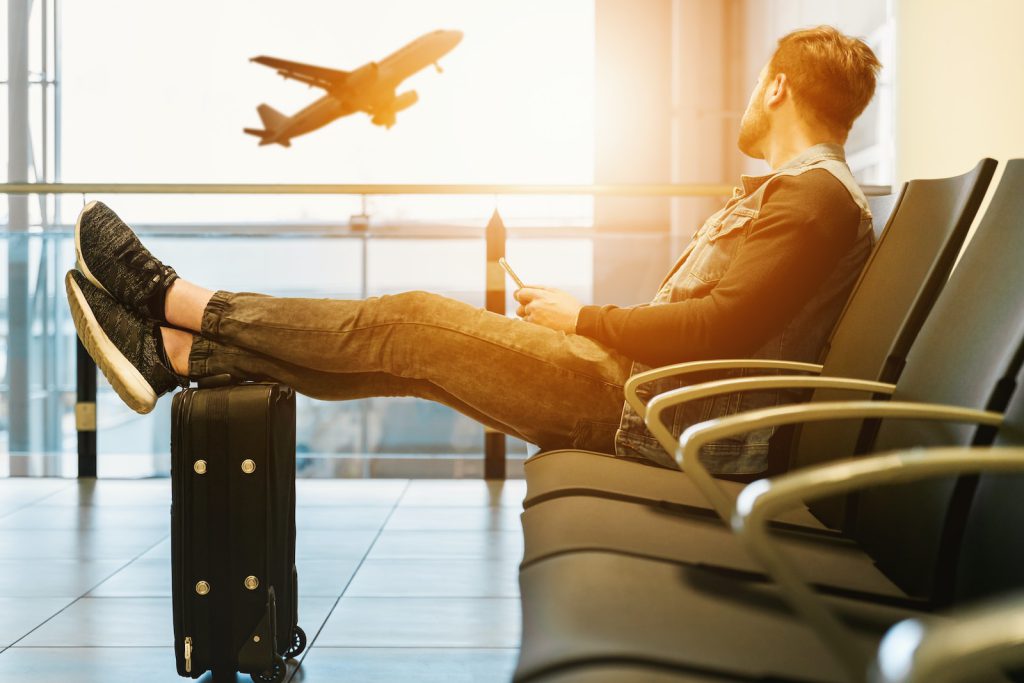 Vliegen zonder kinderen man sitting on gang chair with feet on luggage looking at airplane koffer reizen