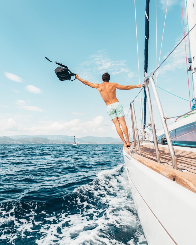 man wearing white shorts holding black backpack vaarvakantie jacht luxe boot zee water